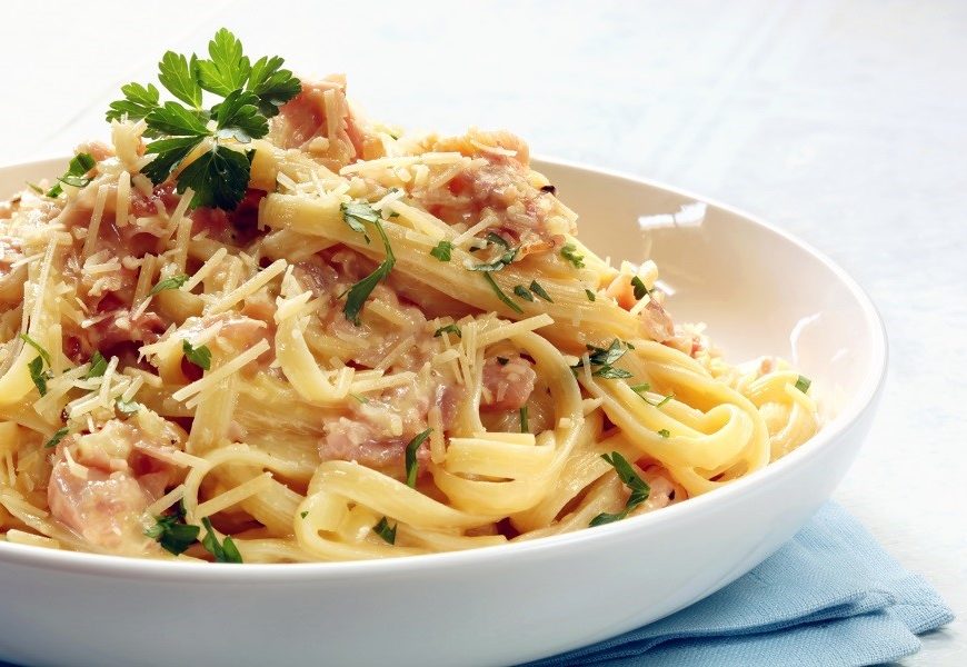 Fettucine carbonara in a white bowl, garnished with parmesan and parsley.